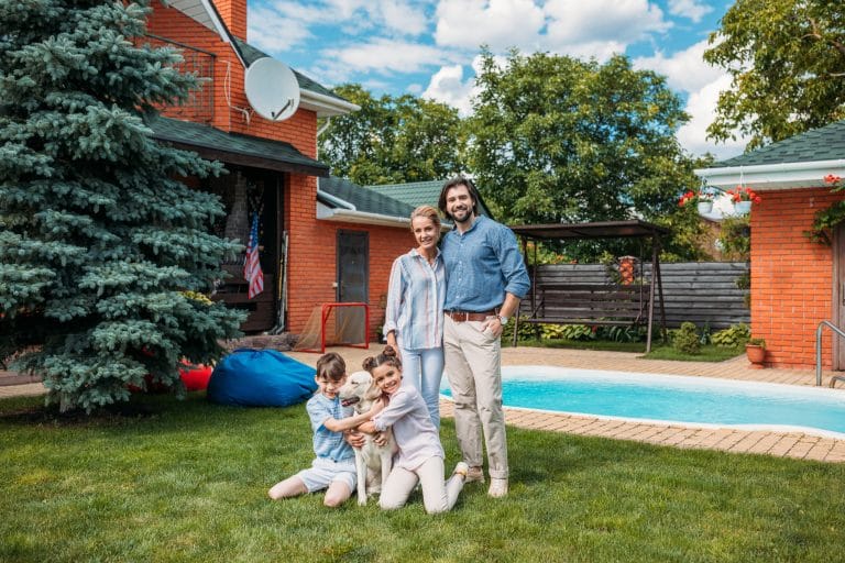 cheerful family with labrador dog looking at camera while spending time on backyard of country house